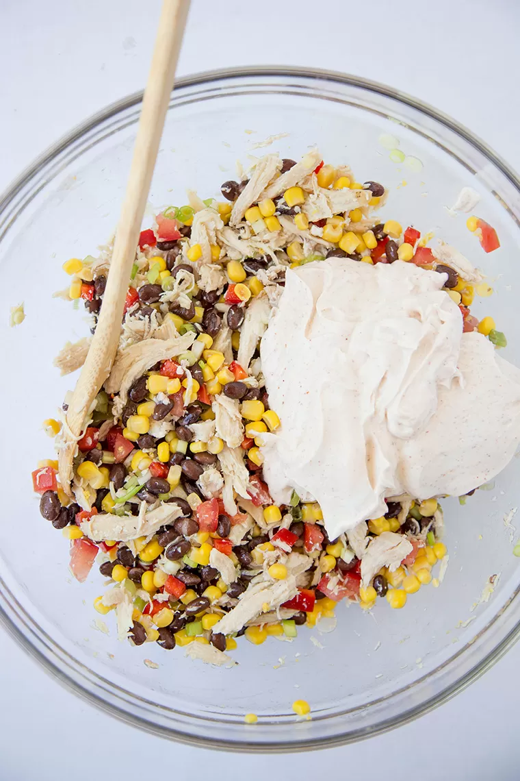 southwest chicken dip ingredients in a bowl with a wooden spoon.