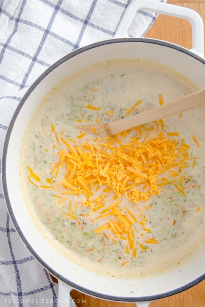 a large pot of broccoli cheese soup with shredded cheddar cheese