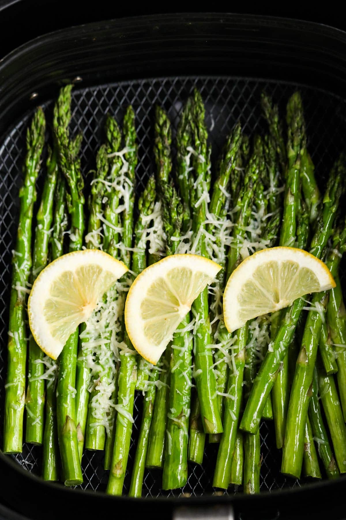 asparagus in air fryer basket with lemon slices and parmesan cheese