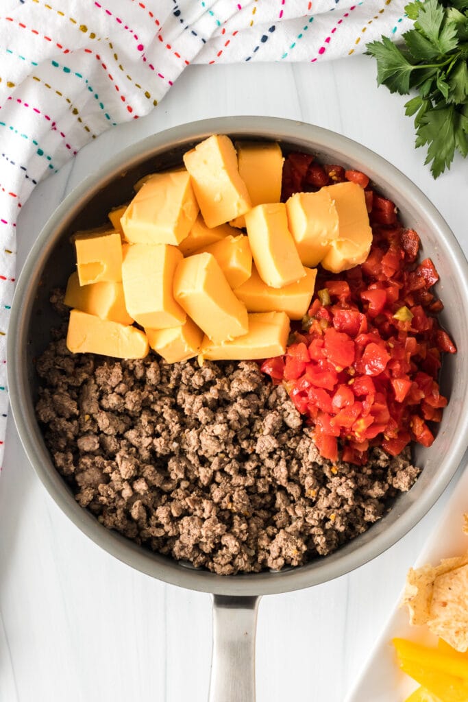 overhead shot of ground sirloin, cubed velveeta, and rotel in a skillet