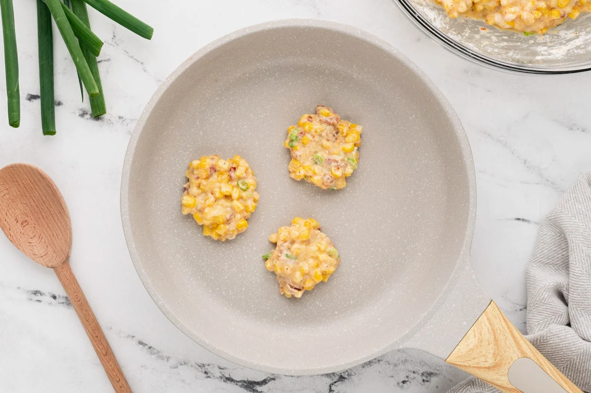 Mini corn cake batter divided into three cakes, in a skillet. 