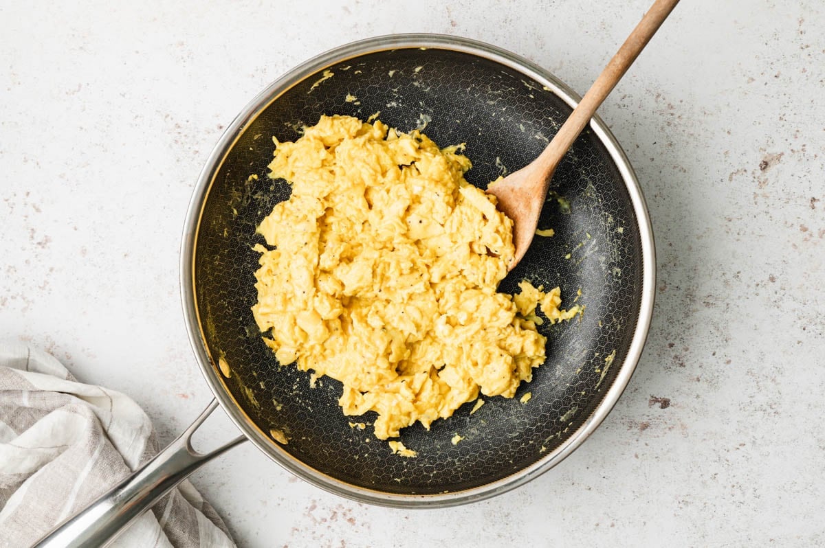 Scrambled eggs in a skillet with a wooden spoon.
