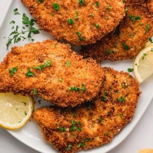 Breaded chicken cutlets, golden and crispy, on a platter with a lemon slice.