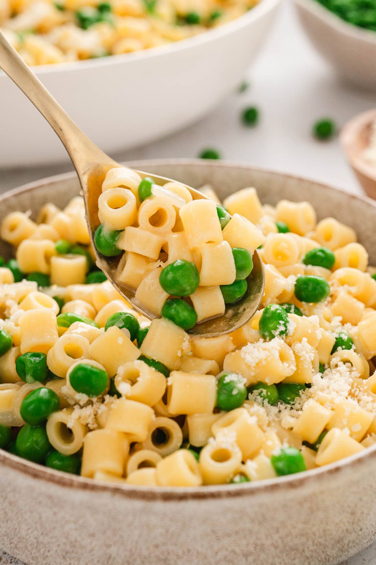 Close up of pasta and peas on a small spoon.
