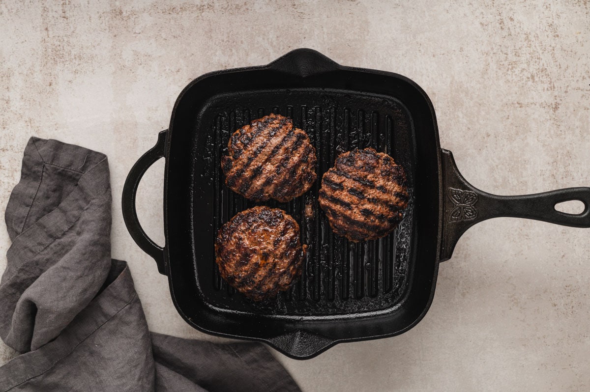 3 grilled hamburger patties on a grill.