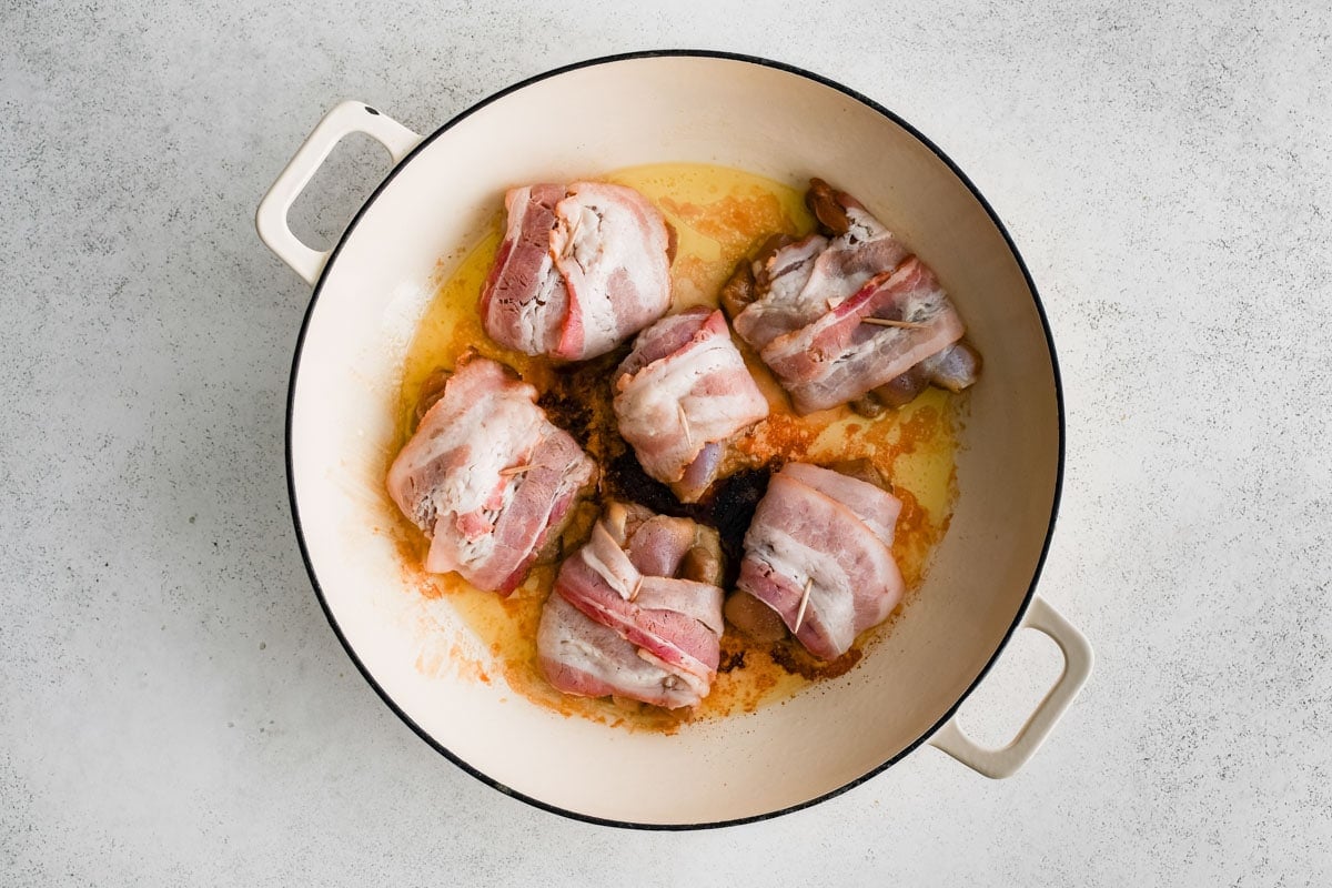 Uncooked bacon wrapped chicken thighs in a skillet,