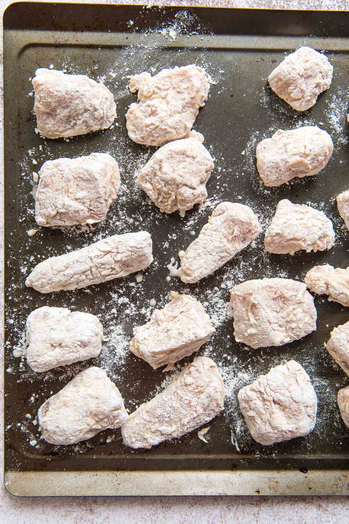 Flour coated pieces of chicken on a baking tray.
