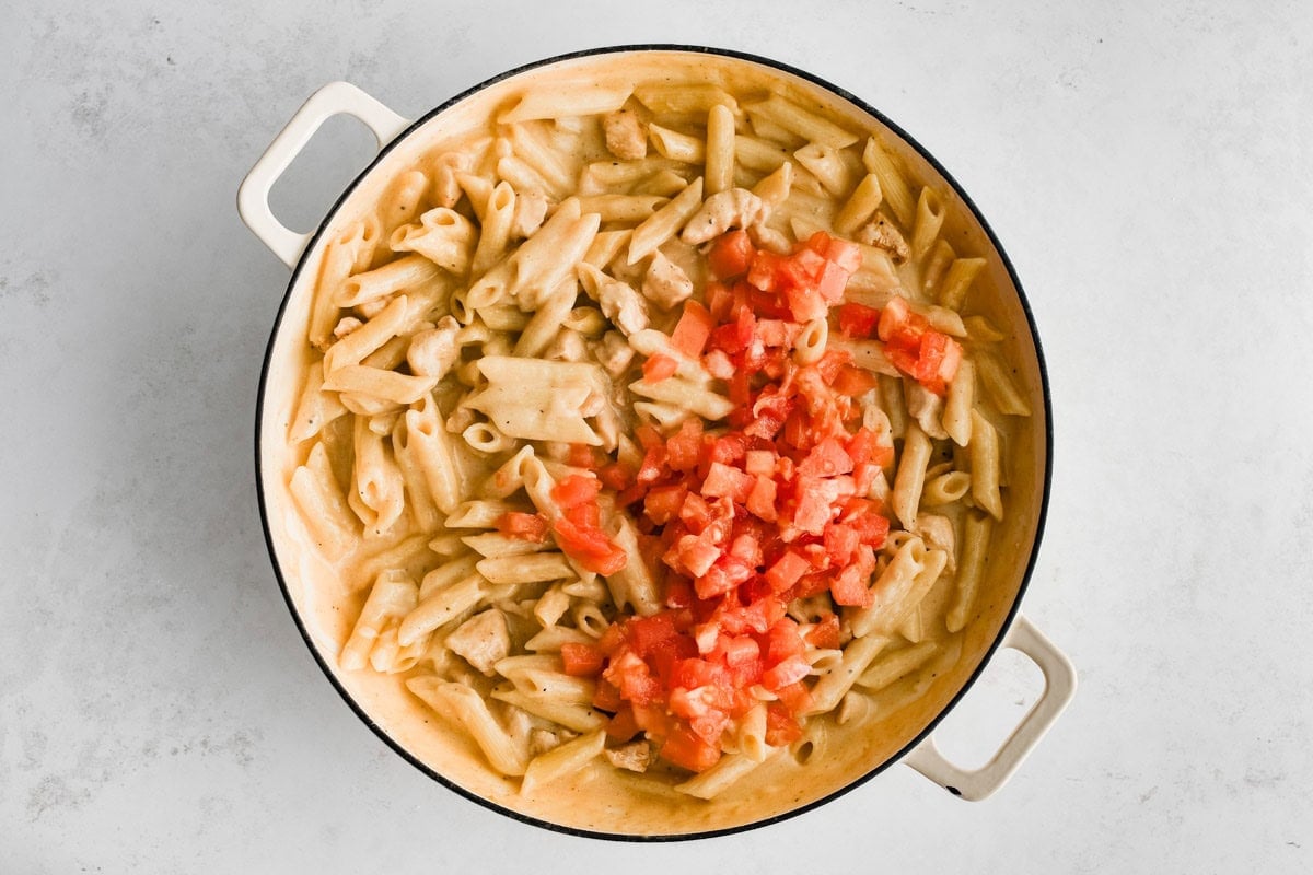 Penne pasta, diced cooked chicken, diced tomatoes in a cajun cream sauce in a skillet.