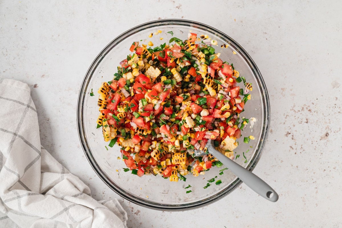 Corn salsa mixed together with a spoon in a bowl,