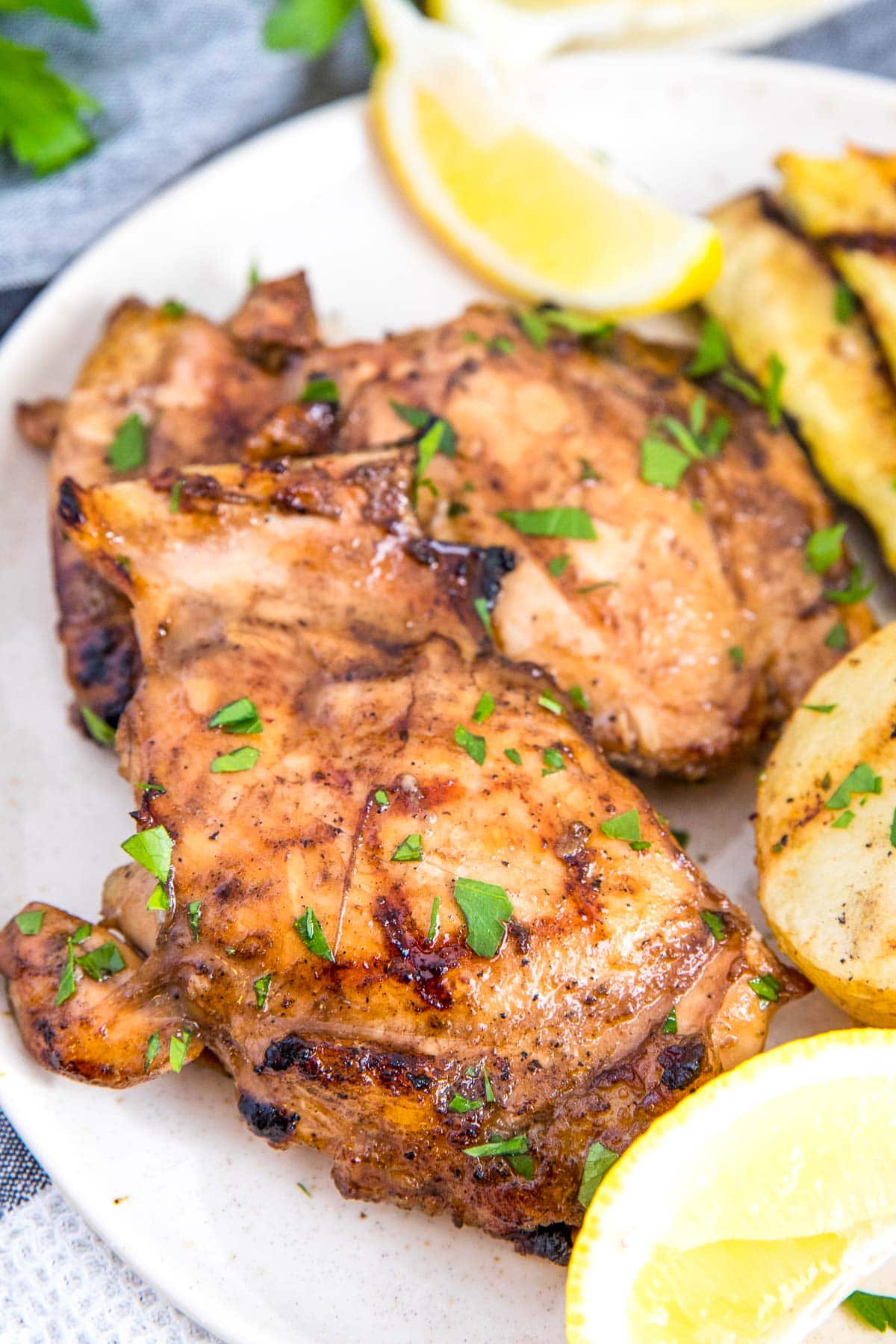 Grilled chicken thighs, potaotes and lemon on a white plate.
