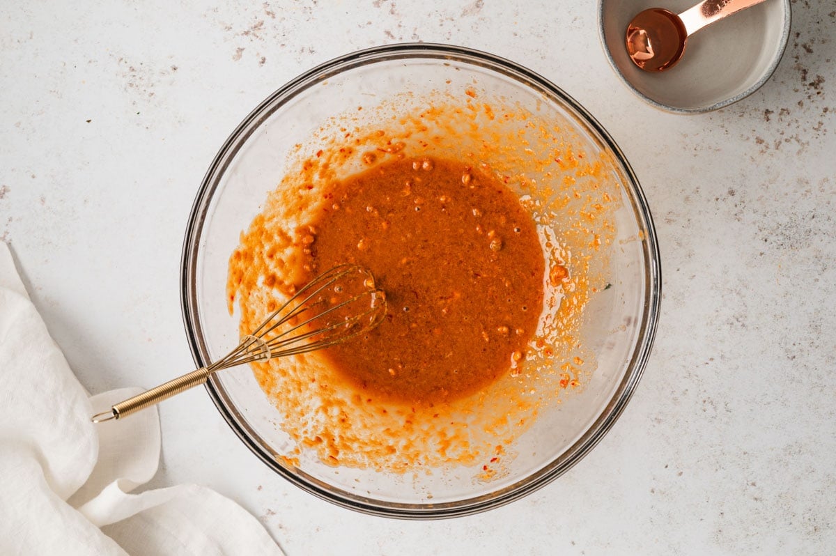 Peanut dressing in a clear glass bowl with a whisk.