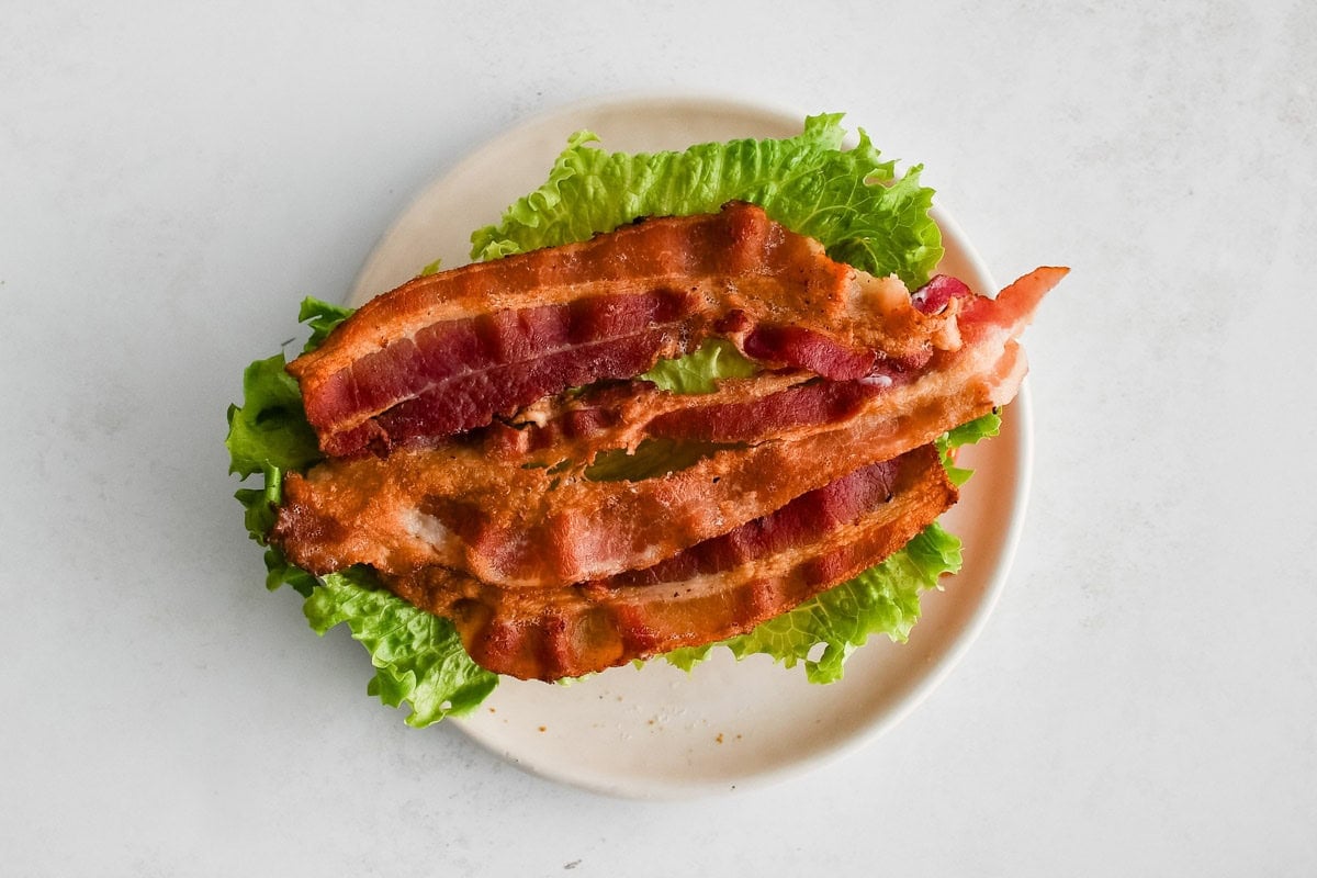 Lettuce leaves and slices of bacon on a plate.