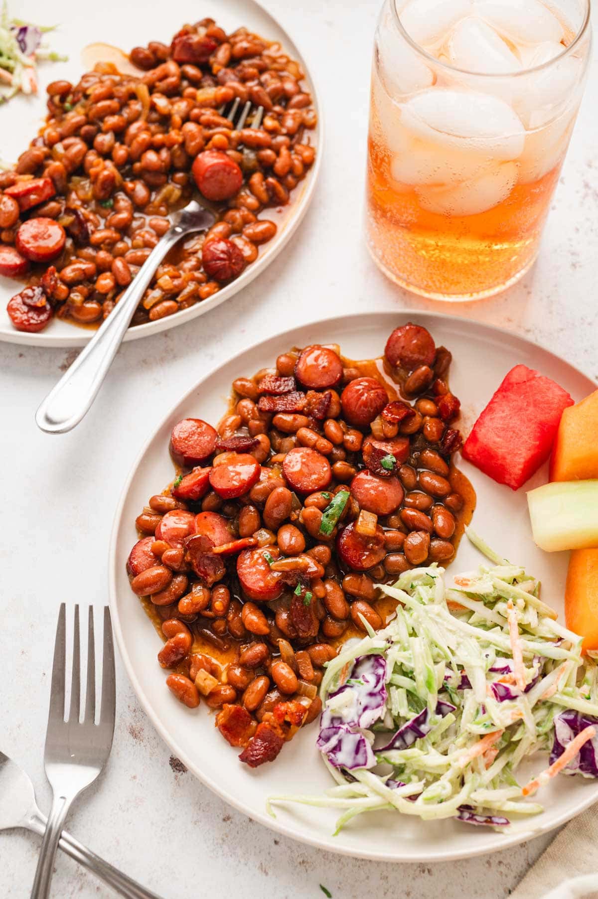 Franks and beans on a plate with diced watermelon and coleslaw.