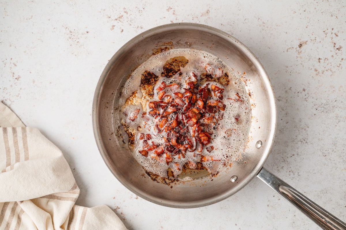 Bacon frying in a silver metal skillet.