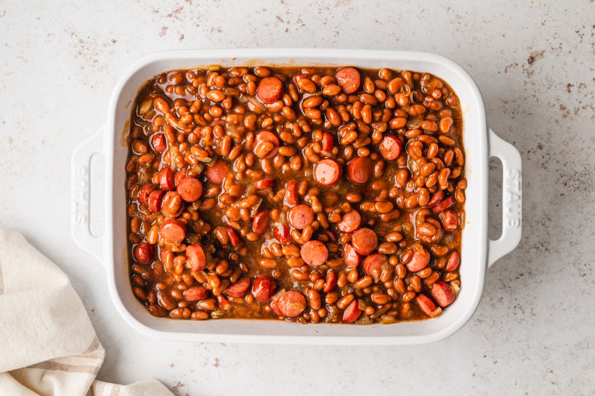 Sliced hot dogs and baked beans in a baking dish.