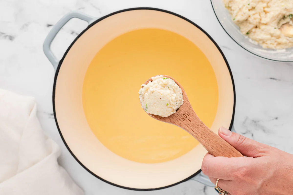 Pot of oil with a spoonful of cornmeal batter. 