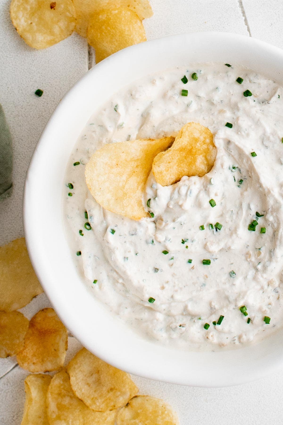 Sour cream and onion dip in a white bowl with potato chips.