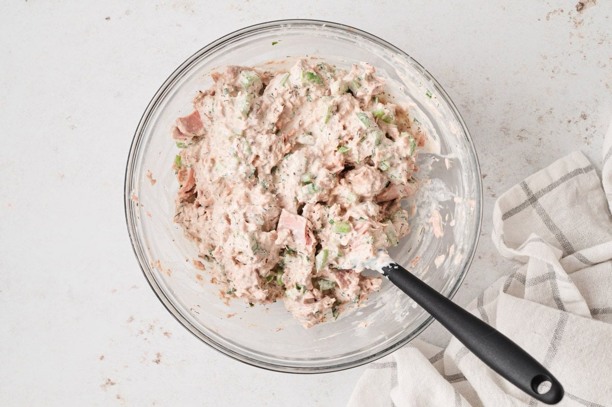 Tuna salad wixed in a glass bowl with a large spoon.