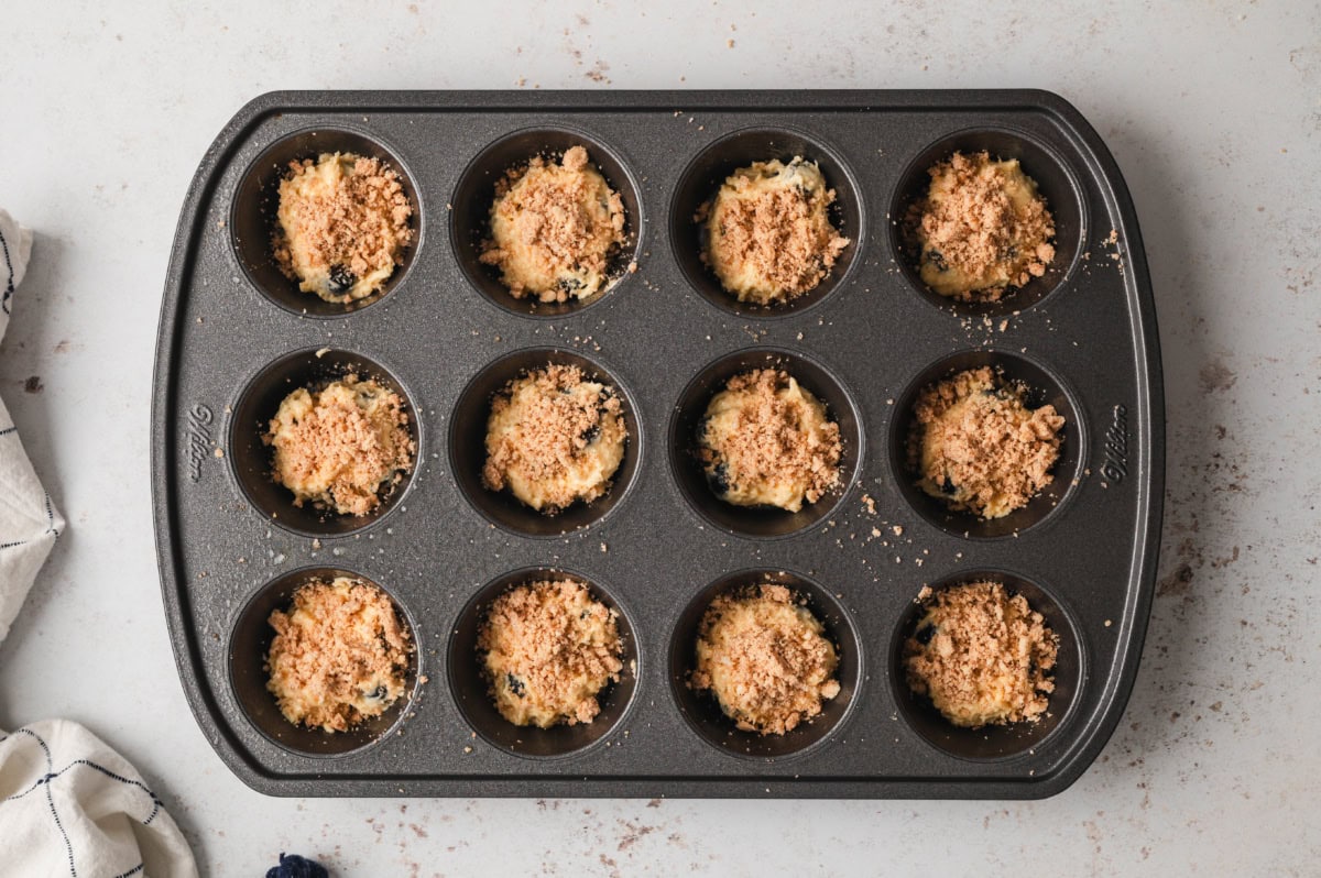 Blueberry muffin batter with streusel topping in a muffin pan.