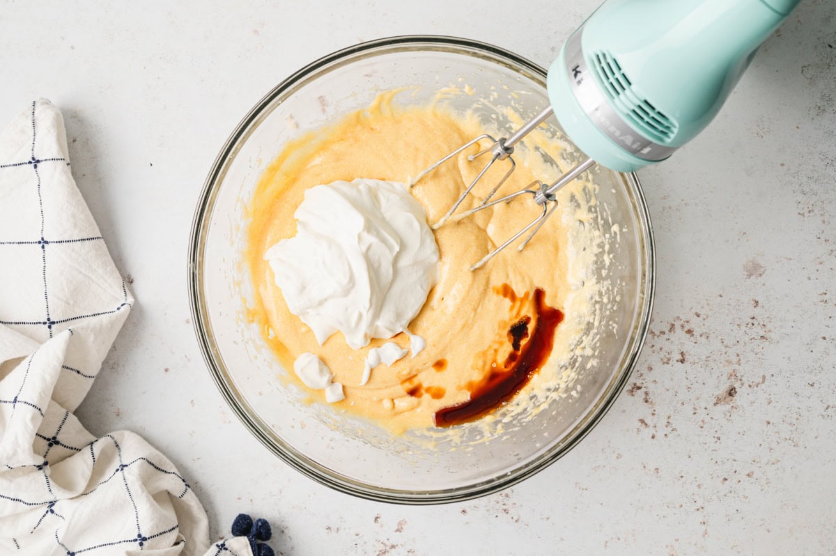 Yellow batter, vanilla and sour cream in a bowl with a hand mixer.