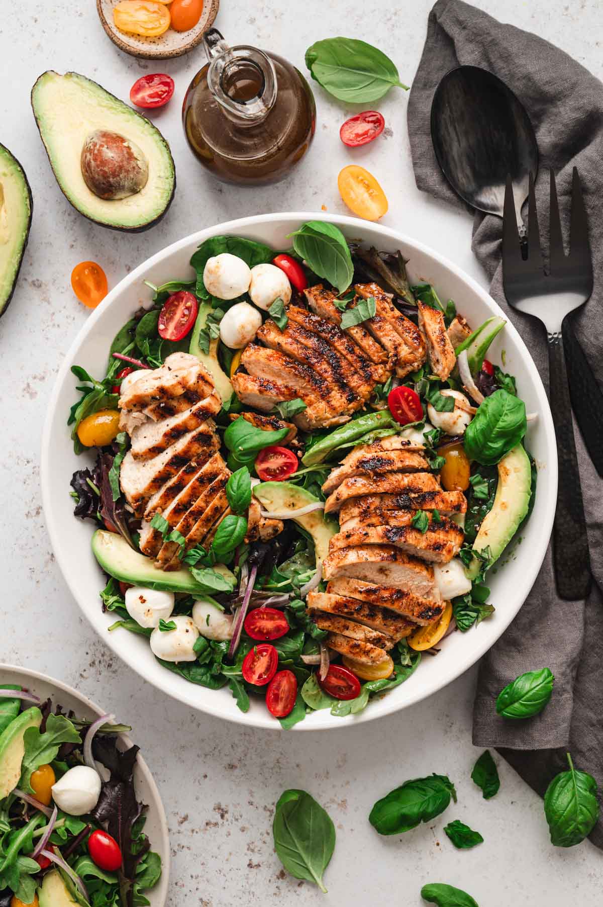 Salad in a white bowl topped with tomatoes, balls of mozzarella, avocado slices and sliced chicken breast.