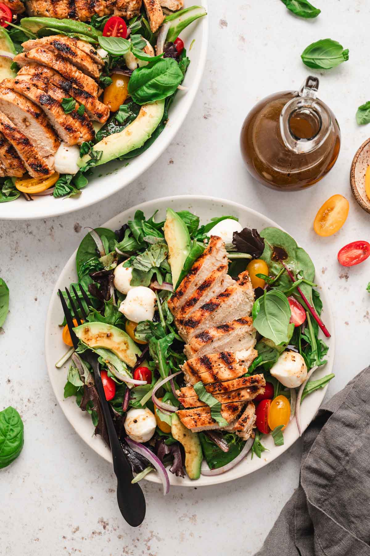 Serving of salad in a white bowl topped with tomatoes, balls of mozzarella, avocado slices and sliced chicken breast.