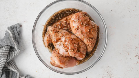 chicken breasts in a marinade in a glass bowl.