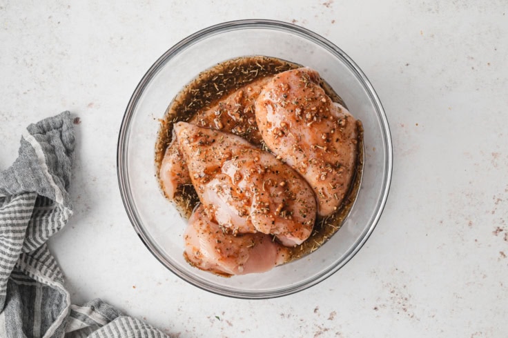 chicken breasts in a marinade in a glass bowl.