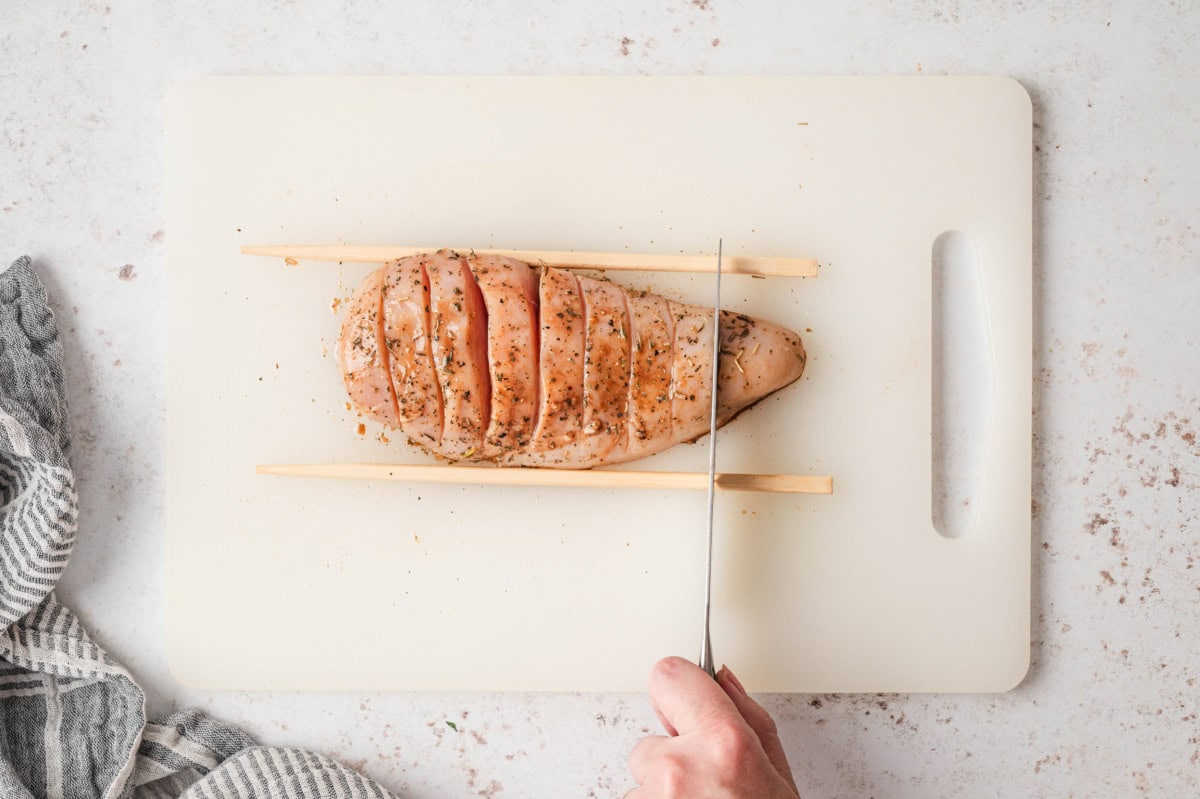 Chicken breast on a cutting board being sliced.