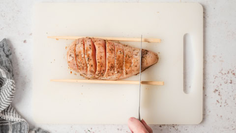 Chicken breast on a cutting board being sliced.