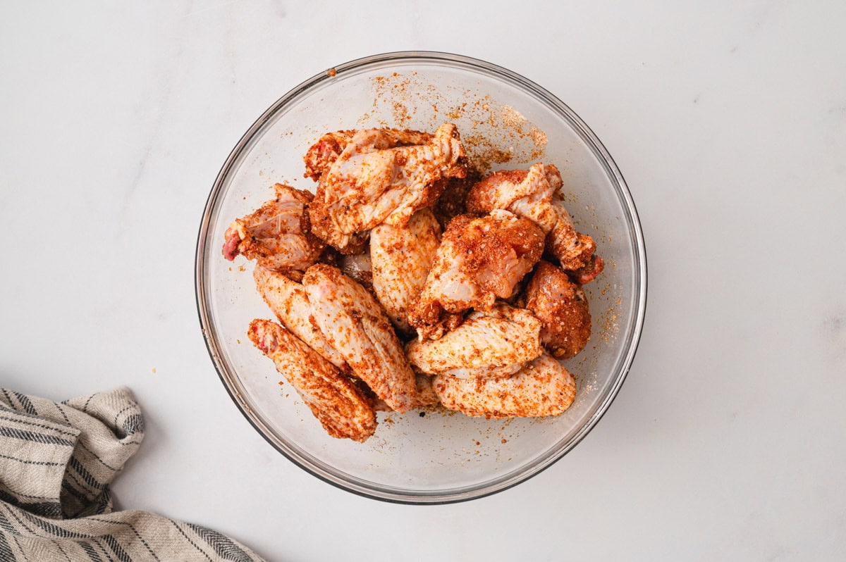 Chicken wings with seasoning in a glass bowl.