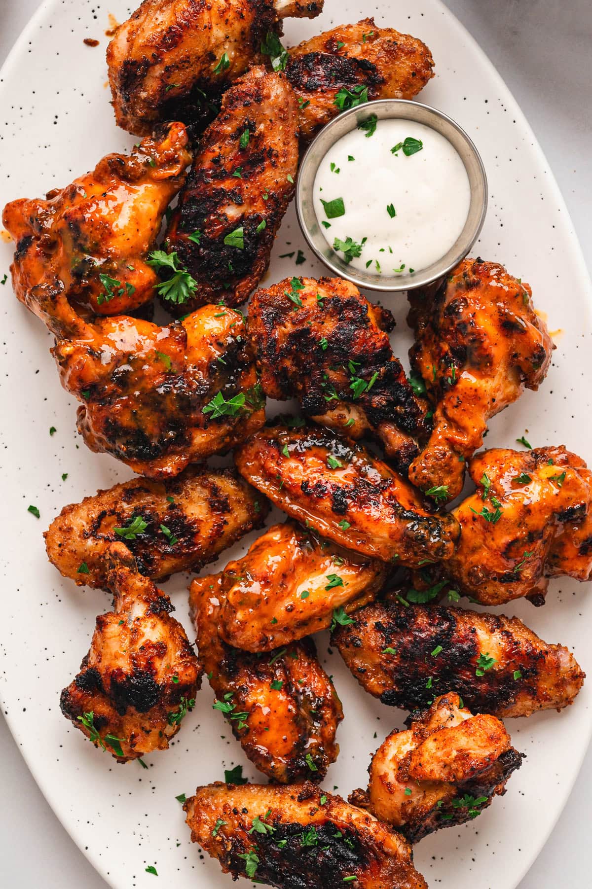 Chicken wings with grill marks arranged on a white platter with a small dish of ranch dip.