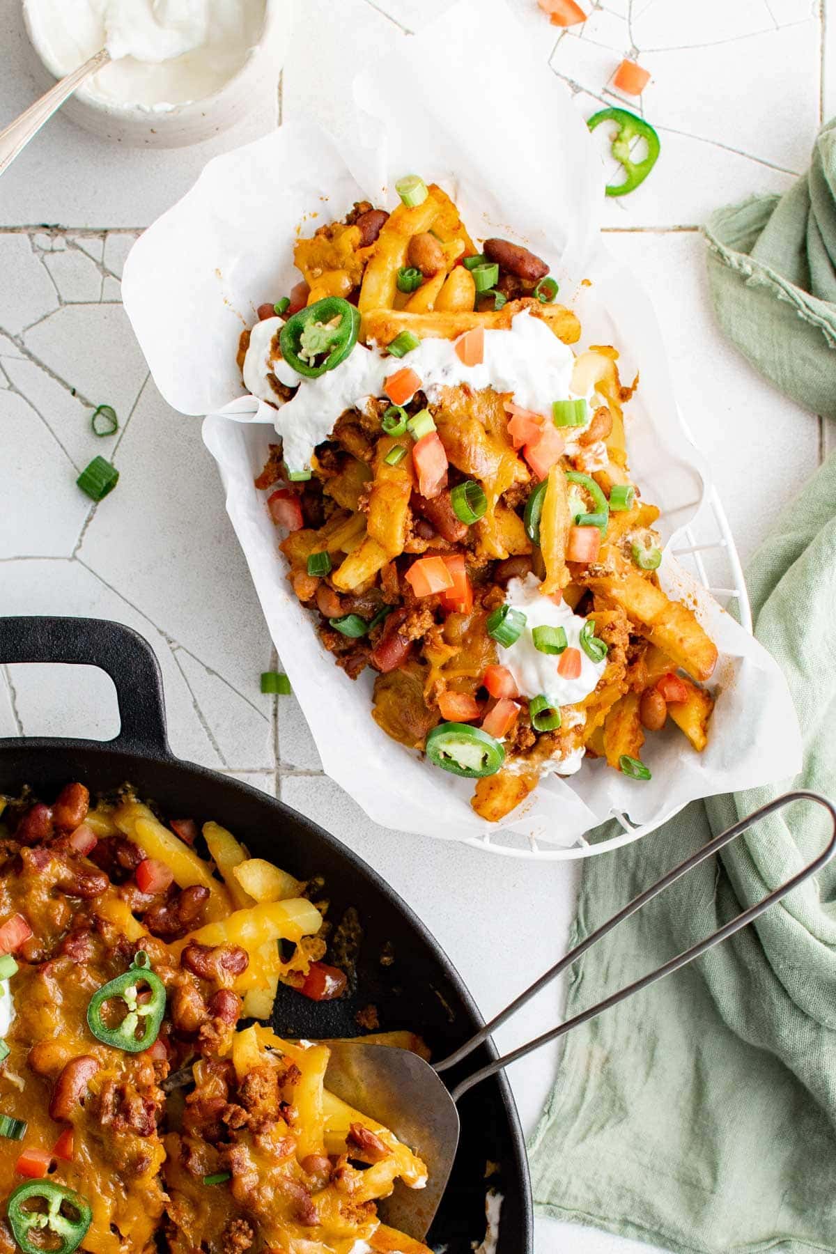 Cast iron skillet with loaded chili and cheese fries, with a second plate with a serving of the fries.