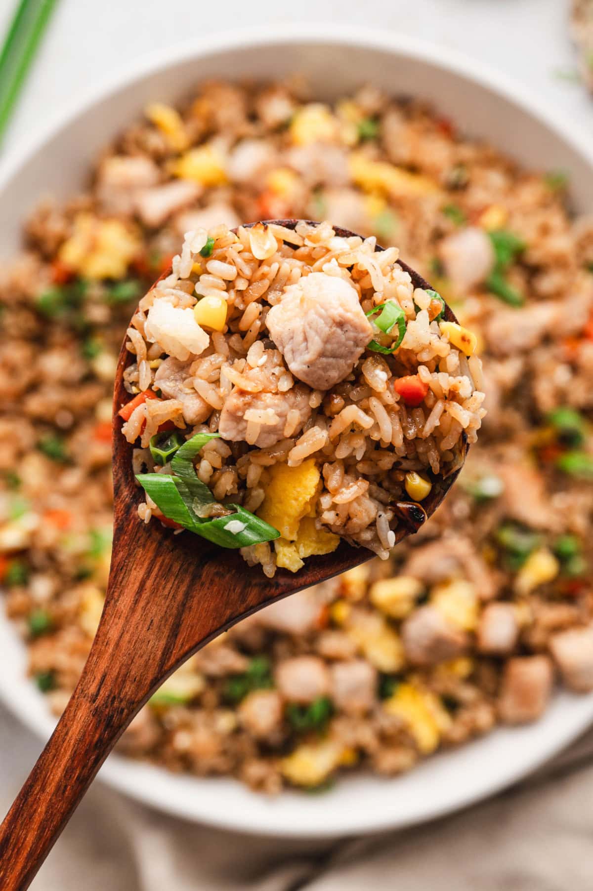 Pork fried rice in a white bowl with a wooden spoon.