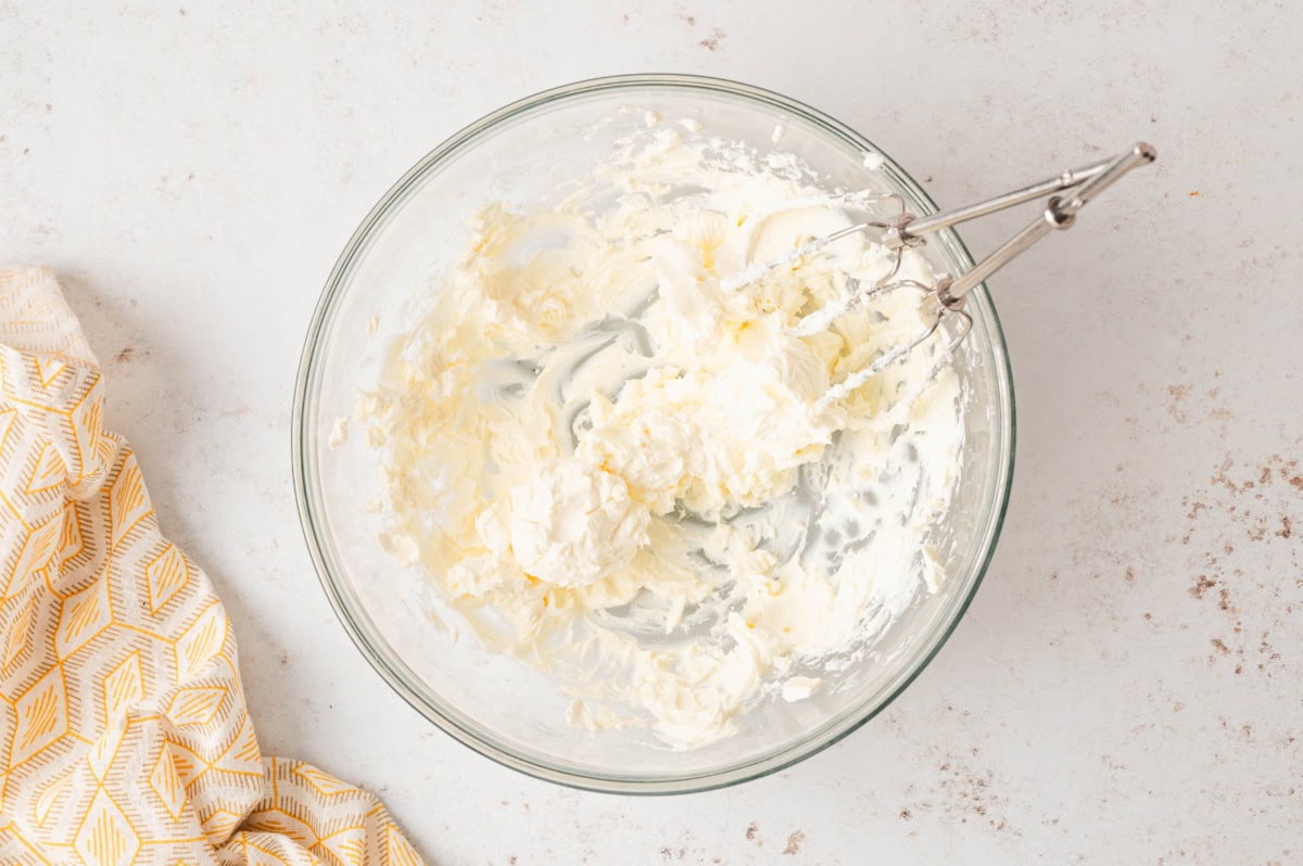 Cream cheese beaten with a hand mixer in a bowl.