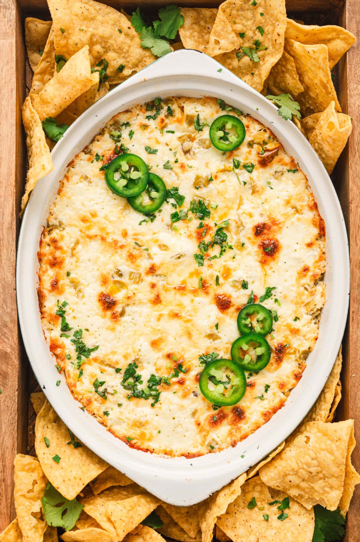 Queso dip baked in a white dish with sliced jalapenos and tortilla chips.