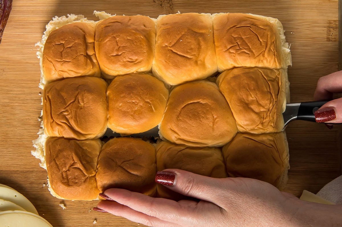 Slider rolls with a hand holding them in place and slicing through them