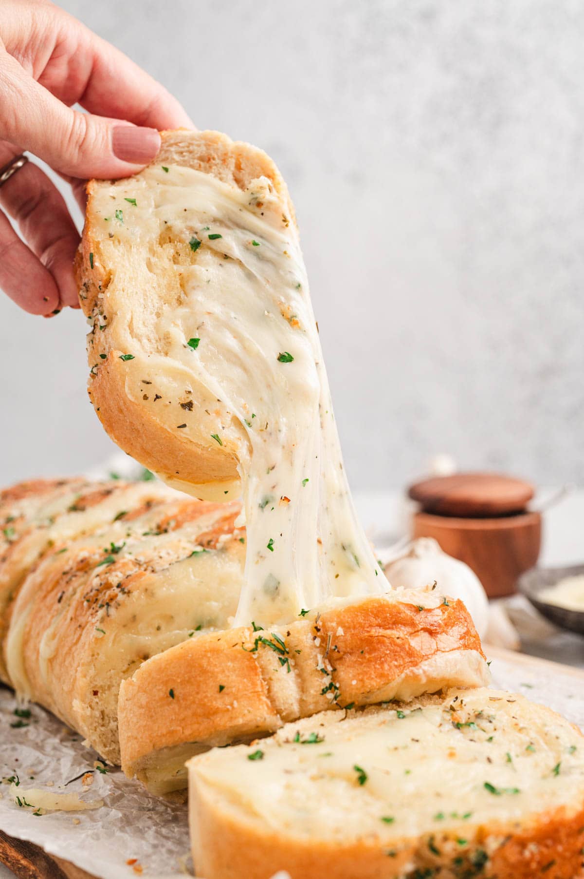 Pulling a slice of cheesy garlic bread out of the loaf of cheesy stuffed garlic bread.