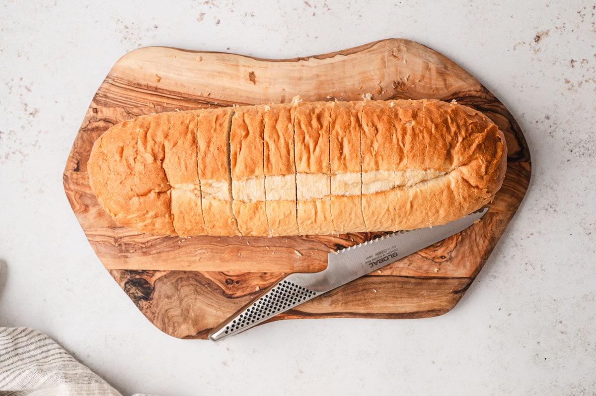 Loaf of italian bread on a cutting board with a knife, with slits throughout.