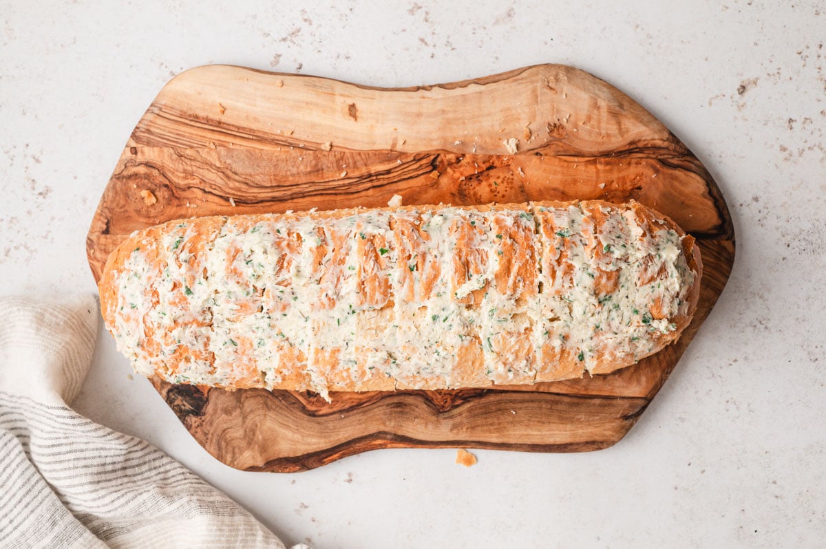 Sliced italian loaf on a cutting board with garlic butter between the slices.