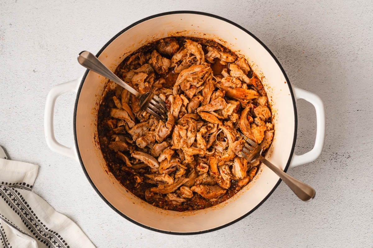 Shredded chicken in chipotle sauce with two forks, in a large pot.