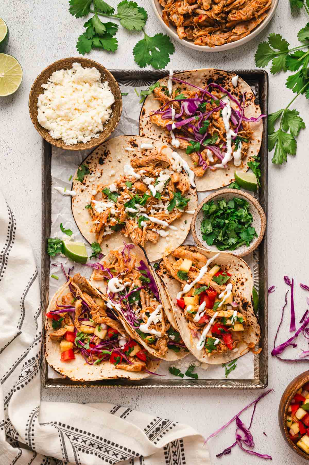 Chipotle chicken tacos with bowls of cotija cheese and diced green onions spread onto a large cookie sheet.