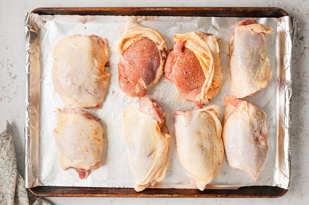 Seasoned uncooked chicken thighs on a sheet pan 