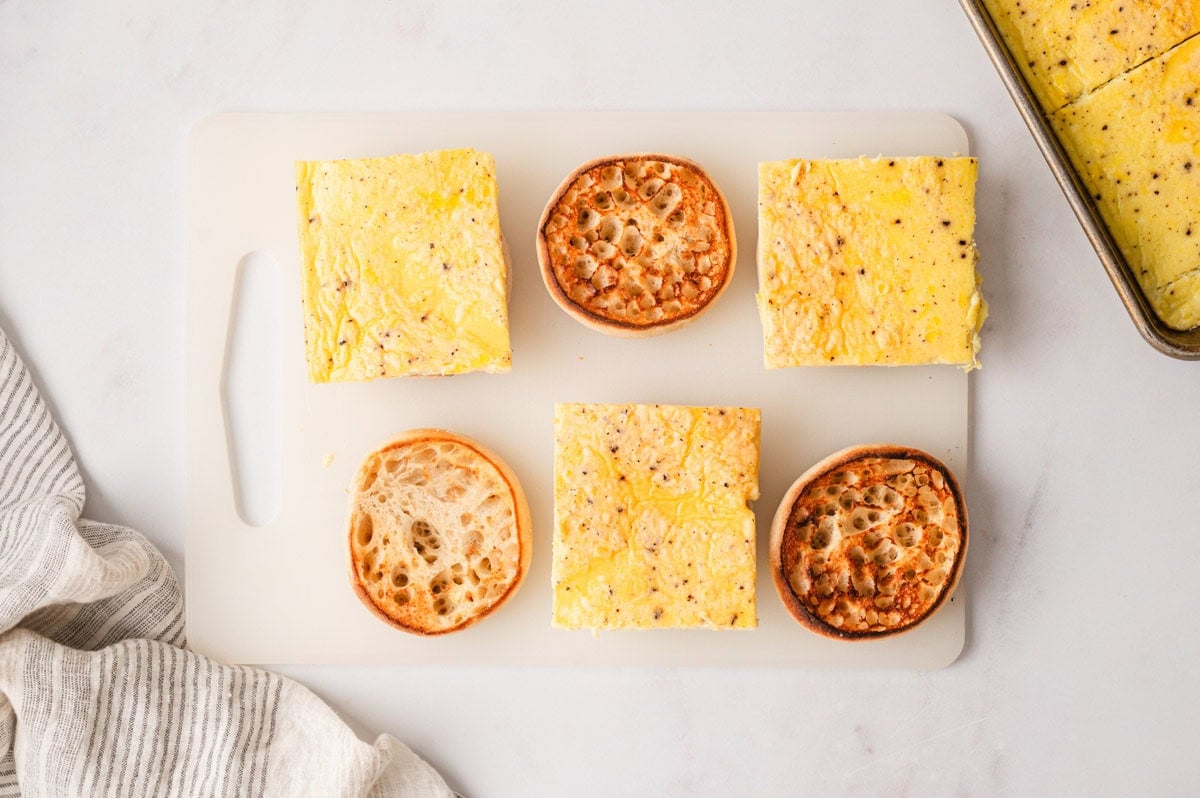 Three open english muffins, and three topped with baked eggs.