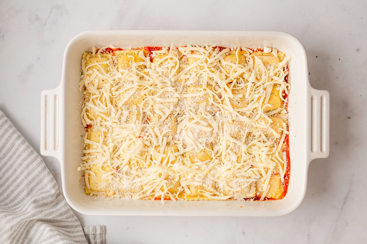 Ravioli covered with cheese in a baking dish.