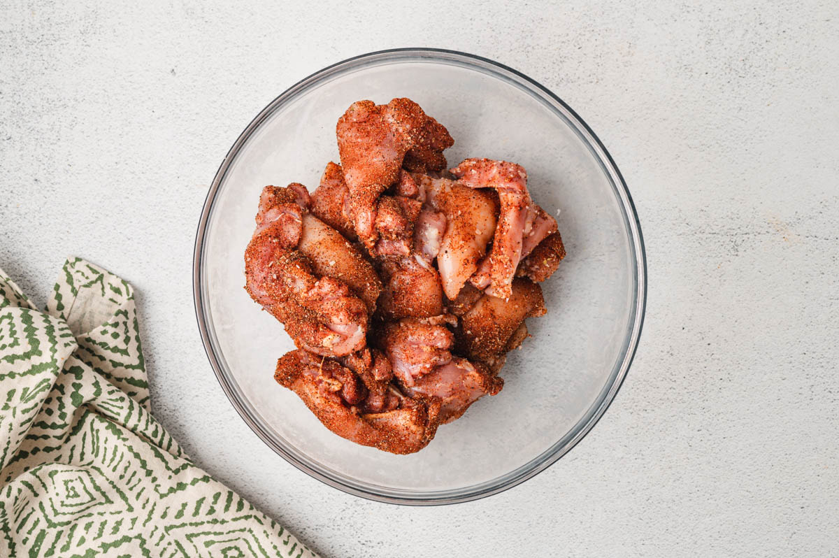 Raw chicken thighs in a glass bowl with taco seasoning.