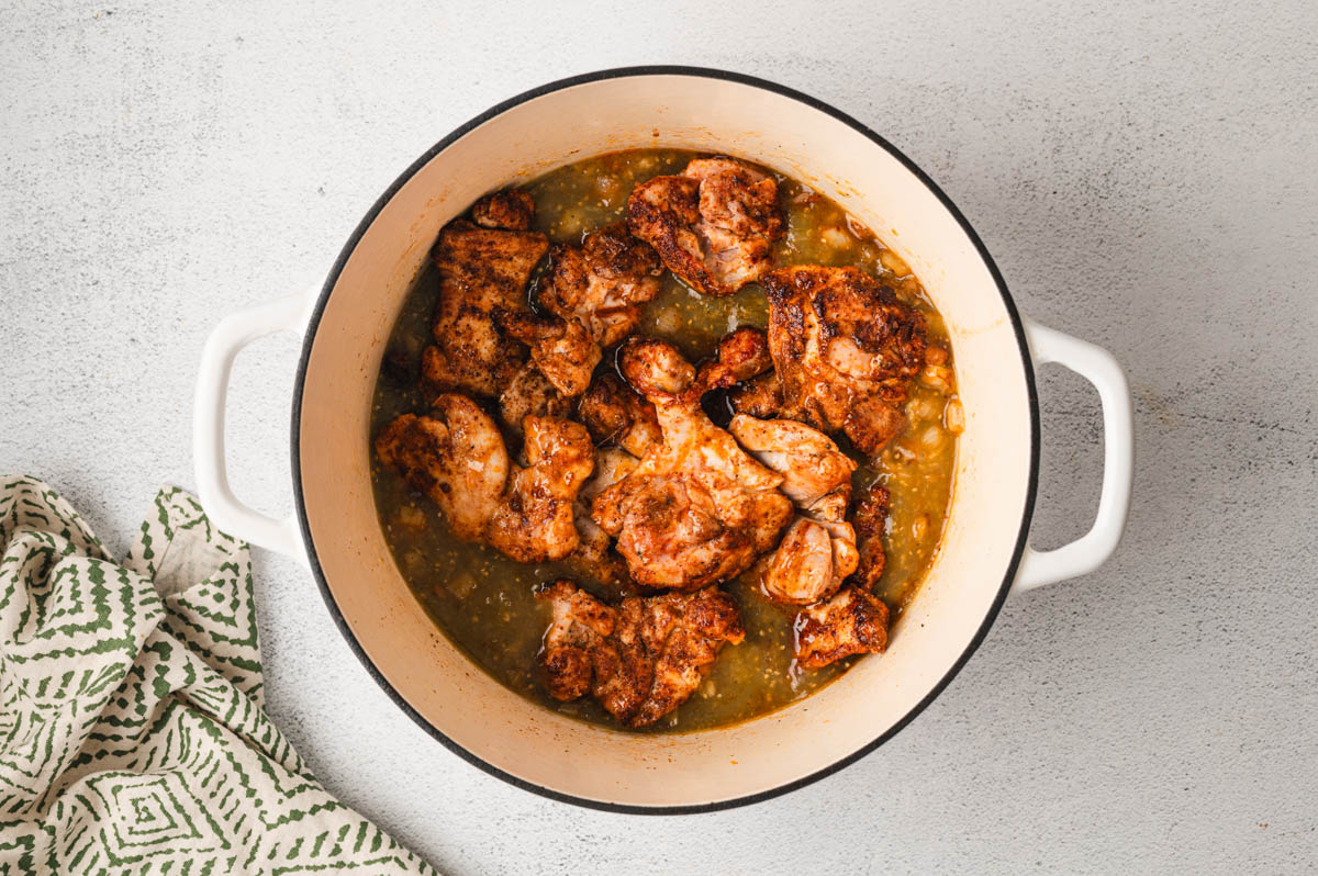 Large pot with seared chicken and green salsa.