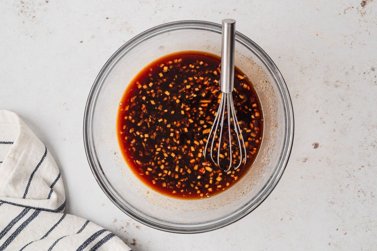 Dark brown sauce in a glass bowl with a whisk.