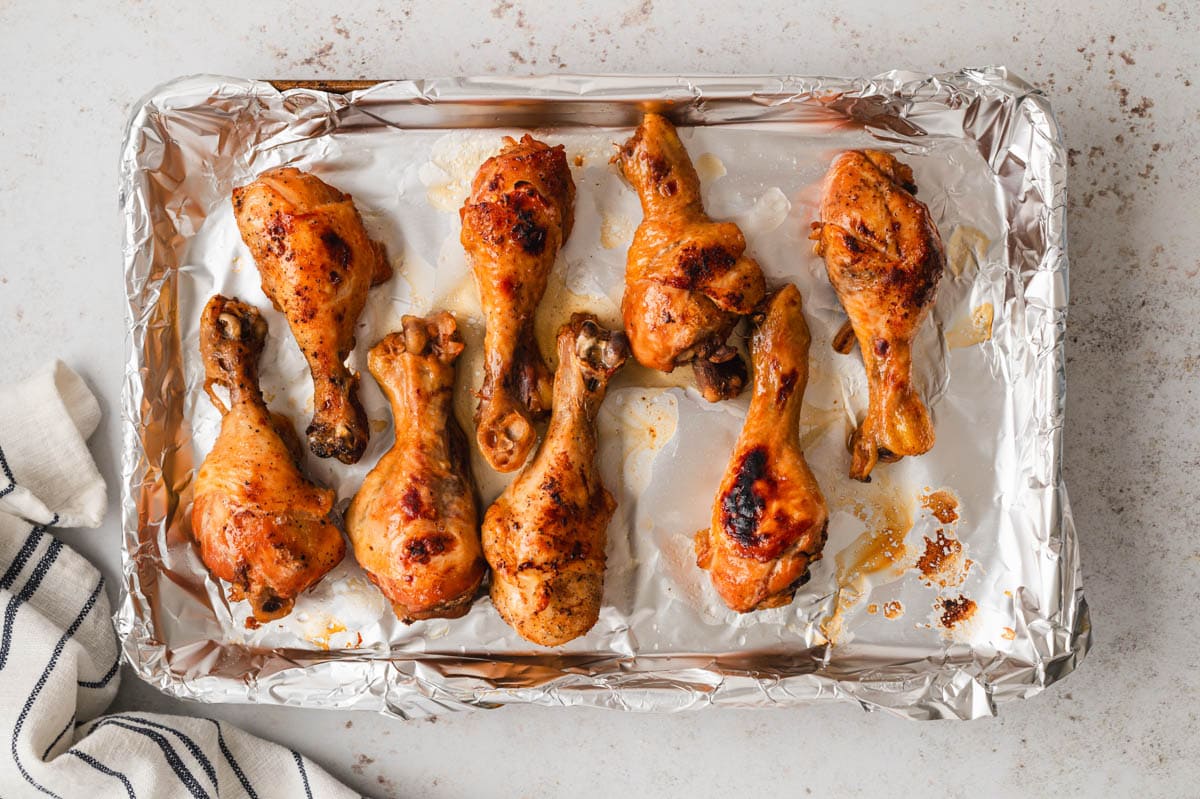 Cooked chicken drumsticks on a sheet pan covered with foil.