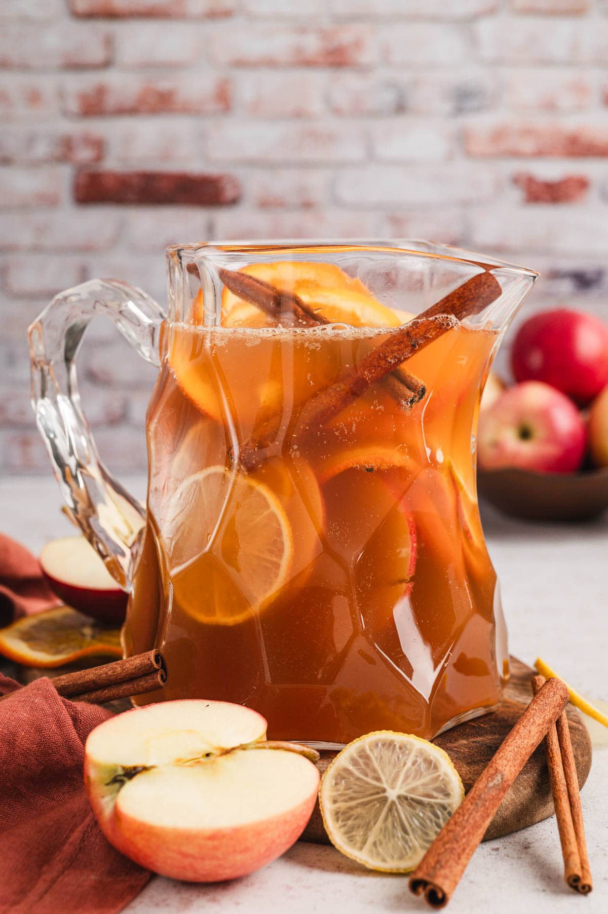 Glass pitcher filled with sliced citrus fruits and apples and apple cider punch.